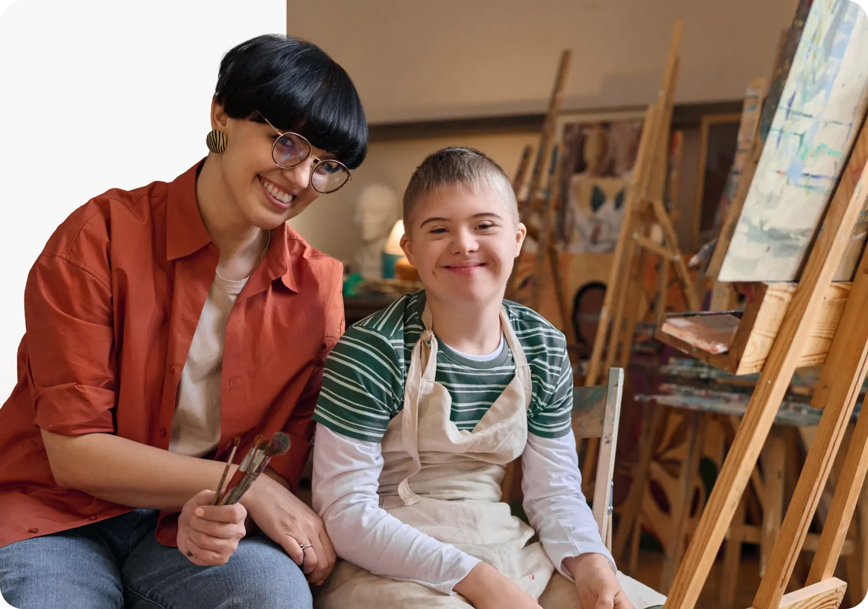 A day program support professional and a participant painting together at an easel in an art studio